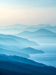 Fototapeta premium Layered Blue Mountain Ranges in Morning Haze Over Water.