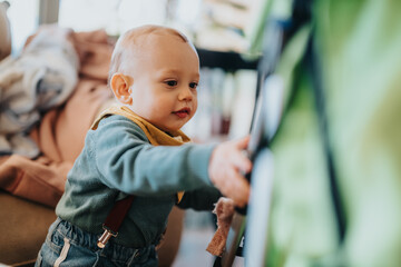 A curious baby dressed in stylish attire interacts with a stroller indoors. The scene conveys a...