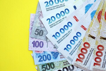 Argentine pesos money bills in big amount lies on yellow color table close up