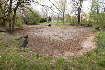 Empty pond in a public park in Dresden, Germany. No water during spring season in 2025. The dried up bottom of the pond is visible.