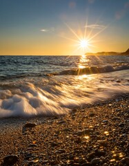 Obraz premium Stunning golden sunset over tranquil waves lapping against a pebbled beach shore.