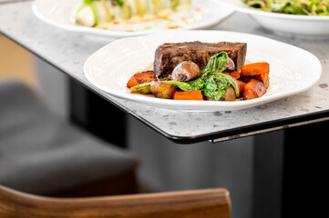 Gourmet dish featuring cooked beef and a medley of roasted vegetables, including carrots, potatoes, and leafy greens. The image highlights vibrant colors and elegant food presentation.
