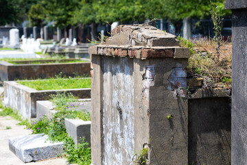 New Orleans raised cemetery with above ground tombstones, angels, and crosses. The graveyard has rich textured tombstones of marble and granite on a lot that is overgrown with ferns and moss. 