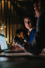Diverse group of coworkers collaborates intensely on a project in a dimly lit office. The...
