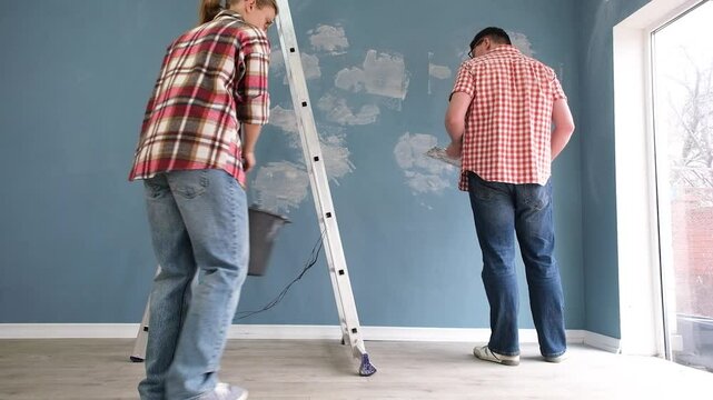 Happy couple renovating new house apartment , spackling wall. Home makeover, renovation concept. Family man woman repair house themselves.