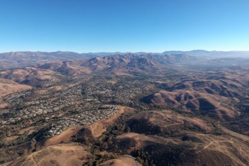 A drone captures a flyer banking left over a lush valley, showcasing crisp terrain details against a clear, expansive sky.