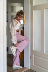 Young modern woman stands oma in doorway, preparing to go out for walk. Girl is dressed in casual clothes, sneakers. Concept of active lifestyle.