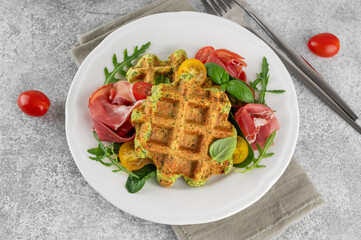 Spinach waffles with tomatoes, arugula and prosciutto on a white plate with a cup of coffee. Healthy breakfast. Top view