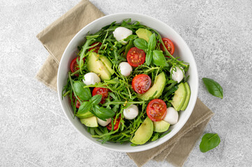 Fresh salad with arugula, mozzarella, tomatoes and avocado in a bowl. Healthy vegetarian dish.