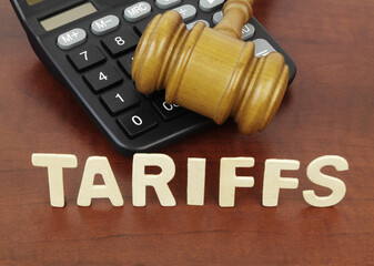 Wooden judge gavel and calculator with word tariffs on table