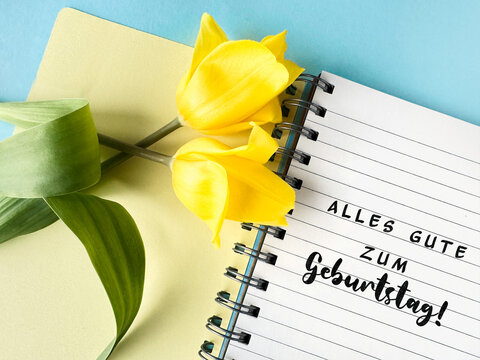 Yellow tulips on a notebook with text Alles Gute zum Geburtstag meaning Happy Birthday in German
