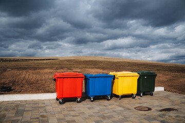 A total of four brightly colored trash cans are neatly arranged in a row along the sidewalk, making...