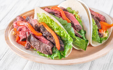 Three carne asada tacos filled with steak, grilled peppers, lettuce, and cheese