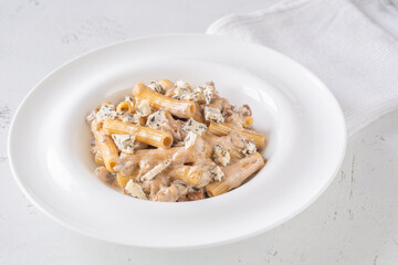 Penne pasta served with creamy walnut blue cheese sauce on white plate