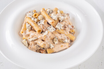 Penne pasta served with creamy walnut blue cheese sauce on white plate