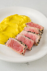 Sesame-crusted sliced tuna with cauliflower curry puree on modern white plate
