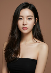 Naklejka premium Portrait of a Beautiful Young Asian Woman with Long Wavy Black Hair, Wearing a Black Tube Top Against a Neutral Brown Background - Perfect for Beauty, Fashion, and Skincare Advertising