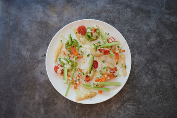 A plate of food with a variety of vegetables including carrots, celery, and broccoli. The plate is white and sits on a grey surface