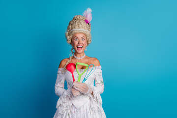 Elegant woman in historical costume holding kitchen utensils against a blue background, blending noble past with playful modern vibes
