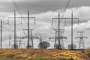 Electric power transmission - overhead high-voltage power lines with metal and concrete supports. The grey sky symbolises problems with electricity supply and energy