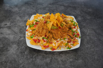 A plate of nachos with meat and vegetables. The plate is white and the nachos are brown