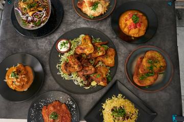 A table with many plates of food, including a plate of chicken wings. There are also plates of rice...