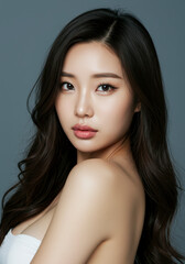 Naklejka premium Stunning Portrait of a Young Asian Woman with Long, Wavy Black Hair and Flawless Skin, Perfect for Beauty, Cosmetics, and Skincare Advertising
