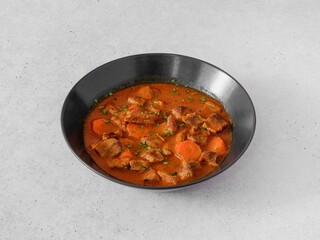 A bowl of food with meat and carrots. The bowl is black and the food is red. There are several pieces of meat and carrots in the bowl