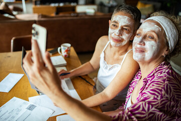 Happy lesbian couple taking selfie with face masks while working from home