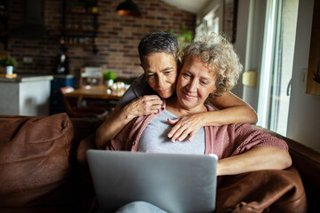 Senior lesbian couple using laptop on cozy couch at home