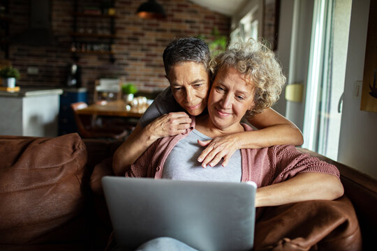 Senior lesbian couple using laptop on cozy couch at home - Powered by Adobe