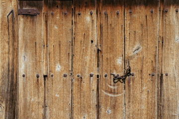 Old wooden door with rusty nails and metal latch, authentic rural craftsmanship. Rustic door reflects ethnographic style, eco-lifestyle, vernacular architecture. Natural vintage background