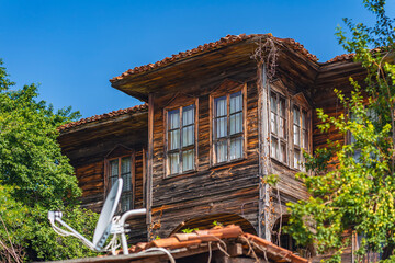 Traditional wooden rustic house with tiled roof and vintage windows in lush greenery. Eco-lifestyle and ethnographic architecture, rural historical environment