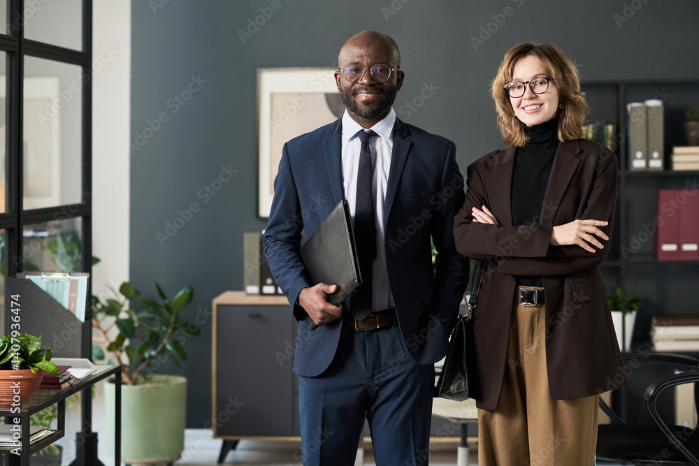 Poster portrait of multiethnic business couple smiling at camera while standing in office