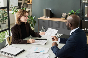 Colleagues sitting at table at meeting and making analysis of financial documents