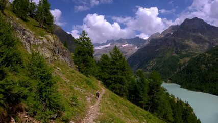 Hiker on narrow trail above turquoise Place Moulin lake italian alps