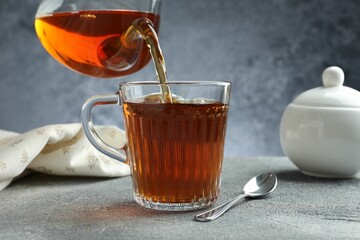 Pouring freshly brewed tea from teapot into cup at grey table, closeup