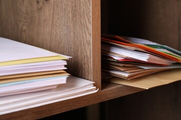Different paper envelopes on wooden shelves in post office, closeup