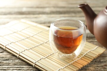 Aromatic tea in cup, bamboo mat and teapot on wooden table, closeup