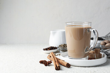 Aromatic Masala tea in glass cup, spices and brown sugar on white textured table, space for text