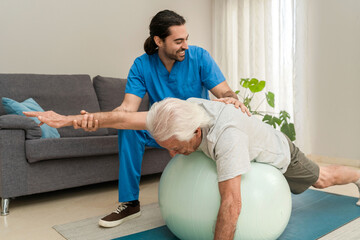 Senior man exercising on fitness ball with physiotherapist at home to improve balance and mobility