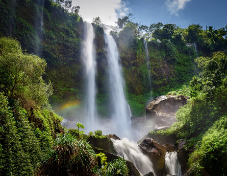 The powerful spray of a waterfall cascading down a rocky cliff surrounded by lush vegetation.