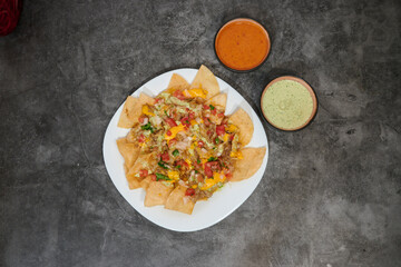 A plate of nachos with a side of guacamole and sour cream. The plate is on a grey counter