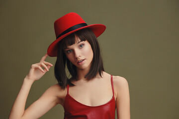 Woman, red hat, leather dress a woman in a red hat and leather dress stands against a green...