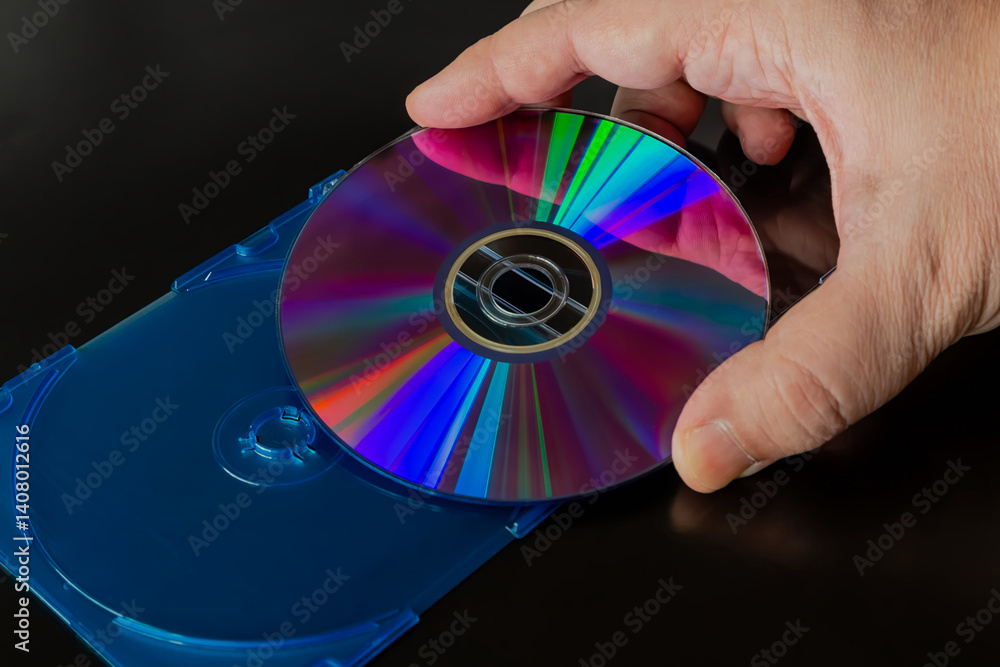 Poster a right hand holding a computer compact disc with rainbow reflections on it above an open disk stora