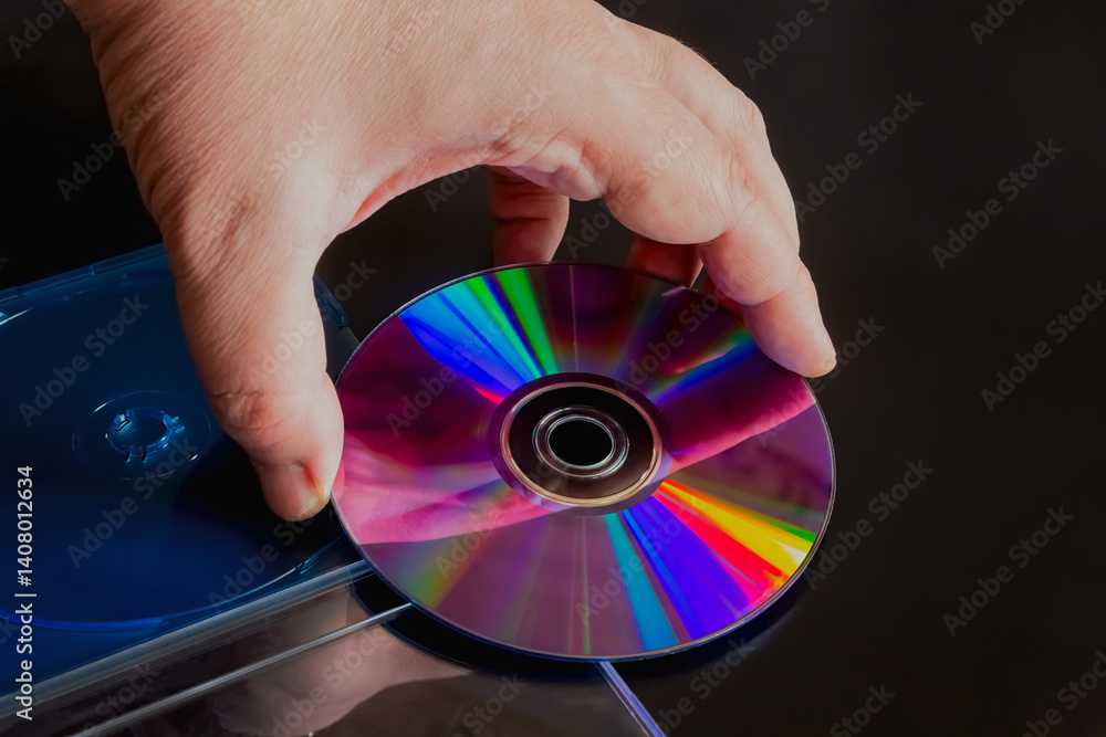 Poster a left hand holding a computer compact disc with rainbow reflections on it above an open case, on a 