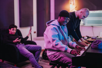 A diverse group of musicians work together in a lively music studio. One plays piano while others...