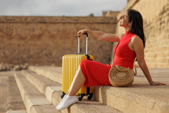Young woman wearing a red dress and carrying a yellow suitcase arrives in the city to enjoy her summer vacation.