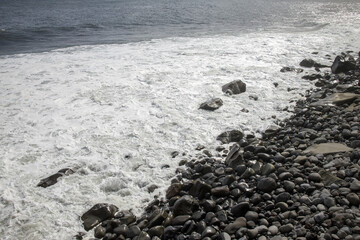 Waves crash against rocky shore at Madeira during a sunny day highlighting the island's natural beauty
