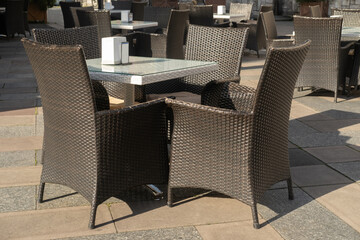 outdoor patio setup, four wicker chairs surround a glass-top table on a stone patio, with napkin holder on the table and similar seating in the background